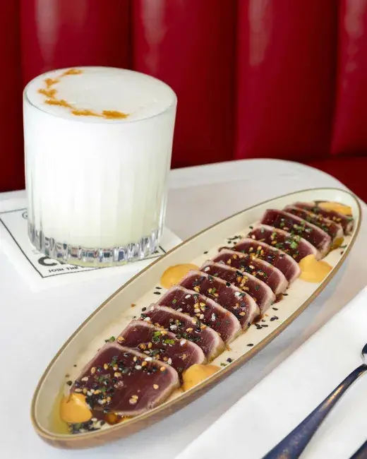 Plato alargado de tataki de atún acompañado de cóctel espumoso.