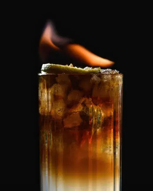 Cóctel con hielo y una rodaja de lima encendida.